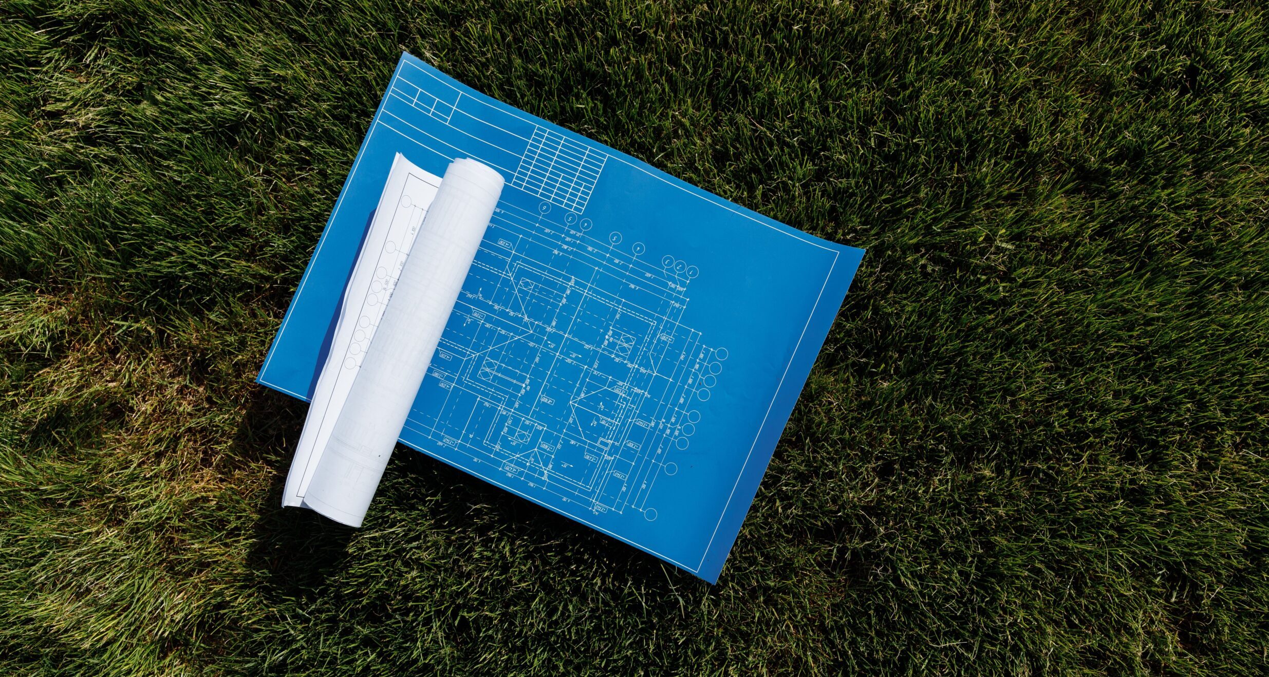 Top view of architectural blueprints on a grassy field, ideal for construction themes.